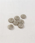 Sept boutons ronds gris grège mats de 14 mm à 2 trous, bord relevé et centre creusé, dont un vu de dos