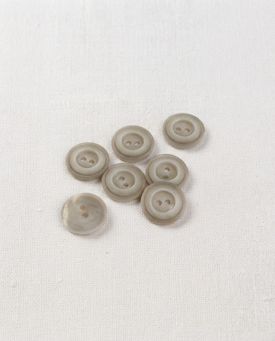 Sept boutons ronds gris grège mats de 14 mm à 2 trous, bord relevé et centre creusé, dont un vu de dos