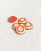 Boutons ronds orange et crème de 18 mm posés en biais, un bouton retourné montre son dos orange
