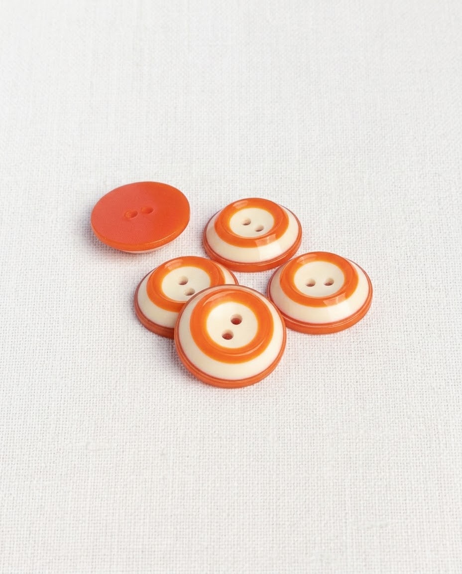 Boutons ronds orange et crème de 18 mm posés en biais, un bouton retourné montre son dos orange