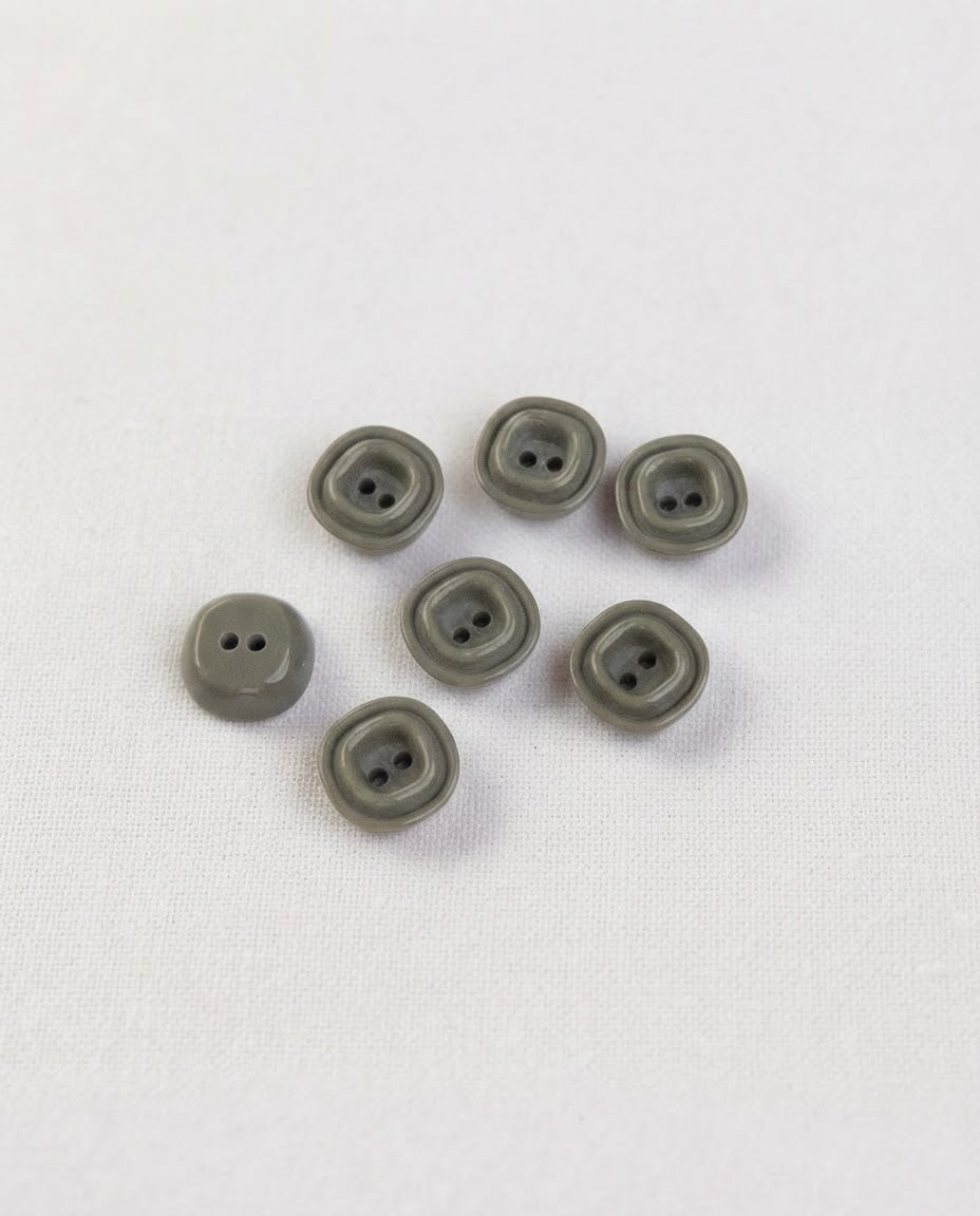 Petits boutons carrés gris vert de 12 mm à 2 trous vus de dessus, un bouton retourné montre son dos bombé