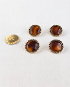 Quatre boutons caramel et doré de 19 mm vus de dessus, à côté d'un bouton retourné qui montre sa queue dorée