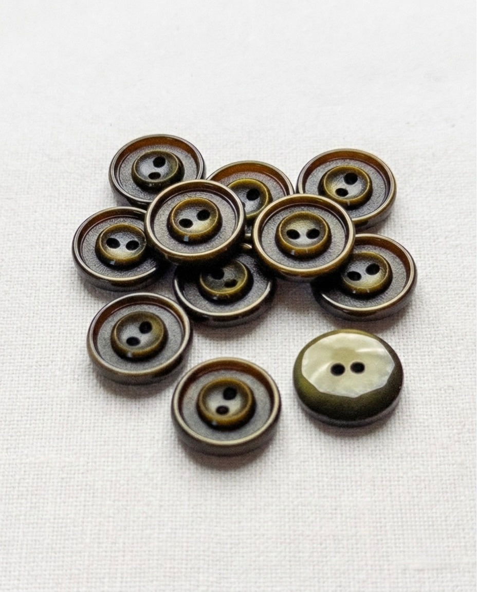 Douze boutons ronds vert olive foncé de 15 mm à 2 trous, anneaux gravés autour des trous, dont un vu de dos marbré