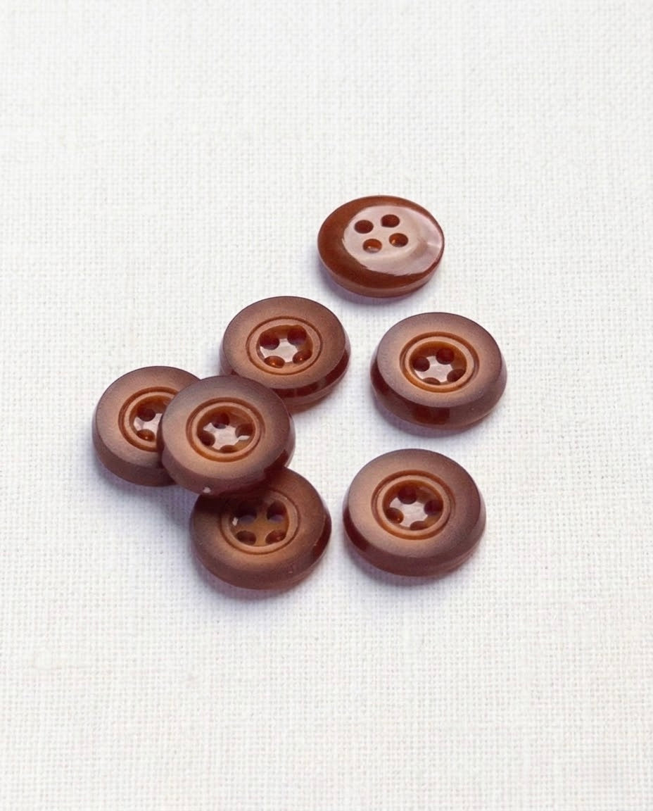 Sept boutons ronds rouille mat de 14 mm à 4 trous, creux en étoile autour des trous, dont un vu de dos brillant