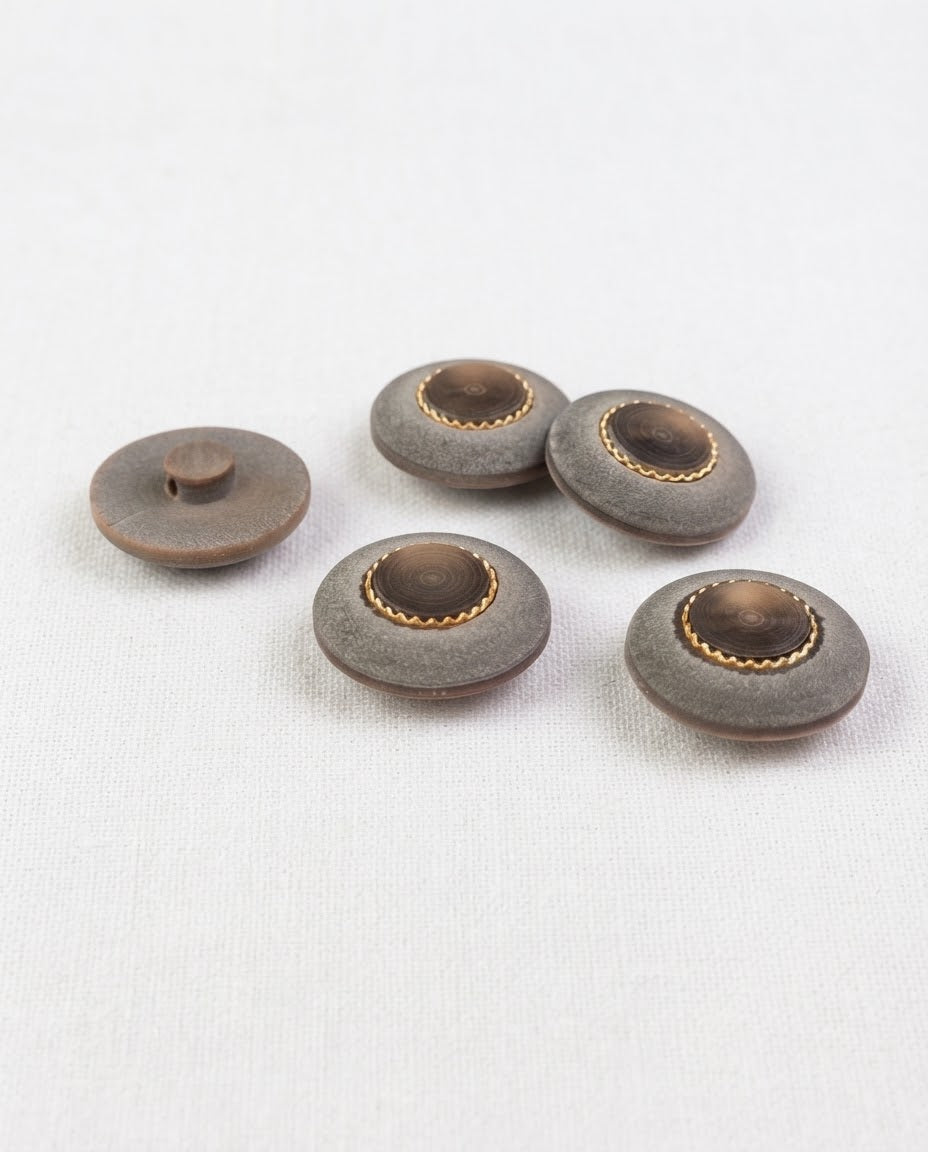 Boutons bombés gris mat de 22 mm à centre brun et anneau doré, posés sur un tissu blanc