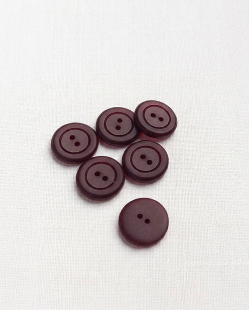 Boutons bordeaux de 17 mm à 2 trous posés sur un tissu blanc, légèrement translucides sur les bords