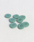 Boutons carrés vert de gris de 17 mm à 4 trous posés sur une toile écrue, dont un vu de dos