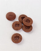 Boutons ronds marbrés brun de 17 mm vus de biais, centre carré en retrait, sur un tissu blanc