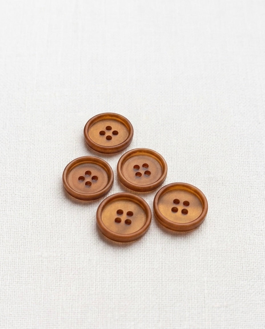 Cinq boutons ronds caramel translucides de 15 mm à 4 trous, avec un rebord, posés sur un tissu blanc