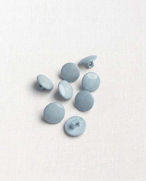 Huit petits boutons ronds bleu clair de 12 mm, bombés et brillants, dont deux vus de profil et un vu de dos montrant la queue