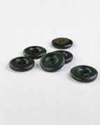 Boutons ronds vert sapin de 22 mm à 2 trous vus de trois quarts, le bord bombé accroche la lumière