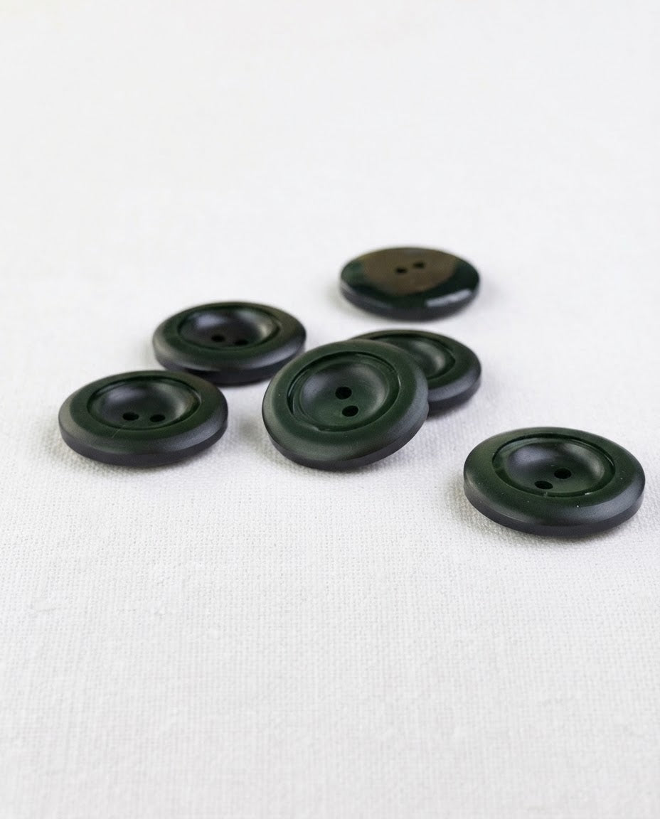 Boutons ronds vert sapin de 22 mm à 2 trous vus de trois quarts, le bord bombé accroche la lumière