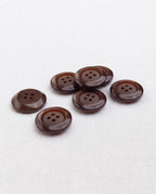 Boutons marron de 17 mm à 4 trous vus de biais, le large bord bombé accroche la lumière