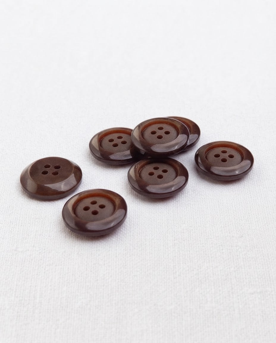 Boutons marron de 17 mm à 4 trous vus de biais, le large bord bombé accroche la lumière