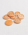 Sept boutons ronds de 18 mm à 2 trous, centre pêche mat, bord crème et fin filet doré, dont un vu de dos pêche uni