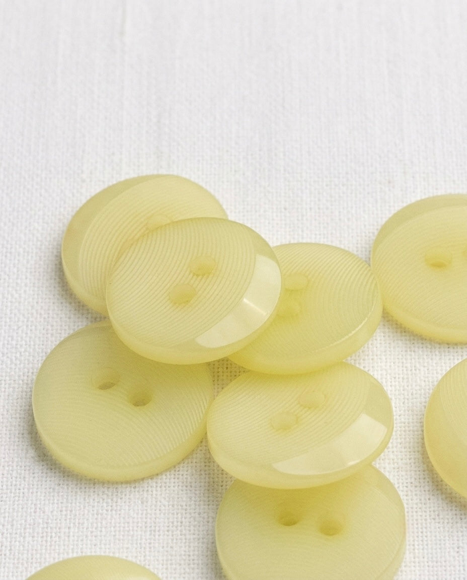 Gros plan sur des boutons ronds jaune primevère translucides de 18 mm à 2 trous, fines rainures concentriques