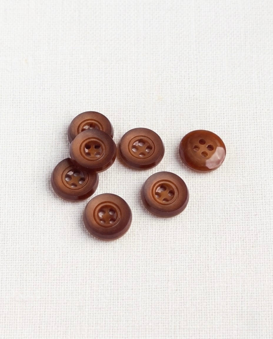 Sept boutons rouille mat de 14 mm à 4 trous vus de dessus, un bouton retourné montre son dos brillant