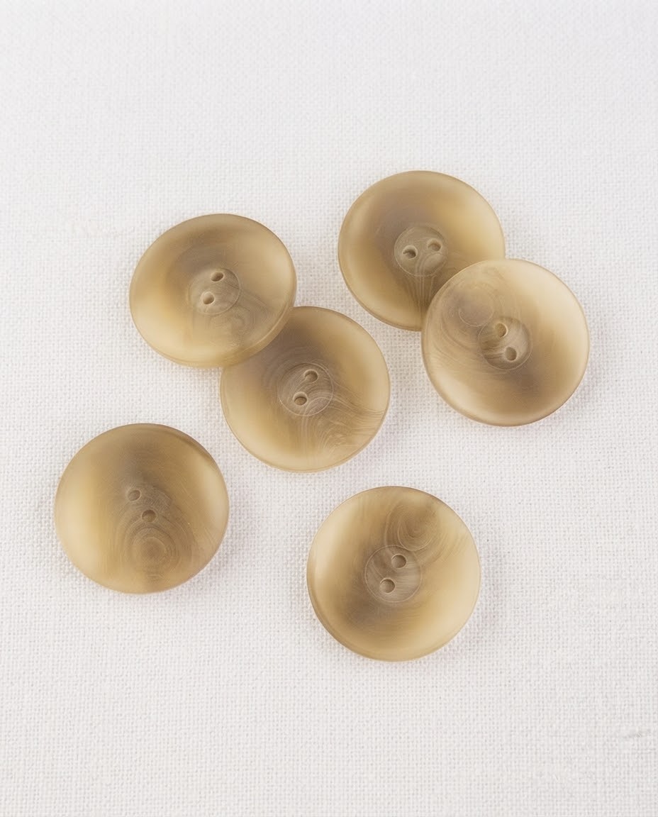 Gros boutons beige doré marbré de 23 mm vus de dessus sur un tissu blanc, surface légèrement creusée